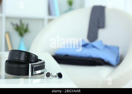Herrengürtel und Manschettenknöpfe auf Kaffeetabellemit Hemd und Krawatte auf Stuhl auf Hintergrund Stockfoto