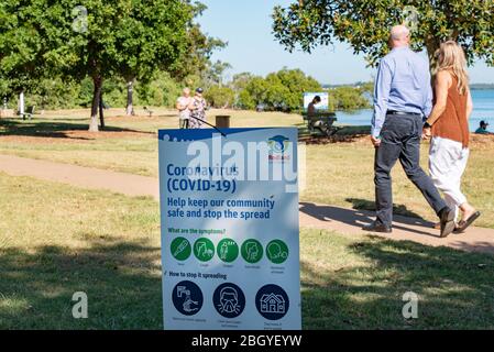 Redlands, Australien. April 2020. Ein Paar geht an einem Schild vorbei, das die Bevölkerung über Covid-19 informiert.Australische Staaten, einschließlich Queensland, halten strenge neue Sperrregeln ein, um die Verbreitung von Covid-19 zu stoppen. Quelle: SOPA Images Limited/Alamy Live News Stockfoto