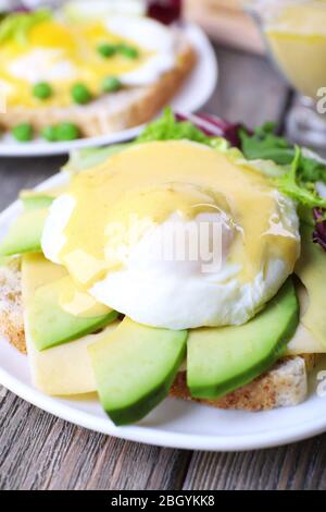 Toast mit Ei Benedikt und Avocado auf Teller auf Holztisch Stockfoto