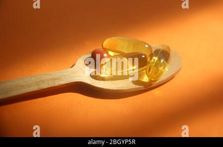 Soft Gele Pillen mit Omega-3-Öl in Holzlöffel auf orangefarbenem Hintergrund unter Sonnenstrahlen. Medizinische pharmazeutische Medizin Konzept Stockfoto