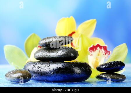 Spa Steine mit Dampf und schöne blühende Orchidee auf blauem Hintergrund Stockfoto