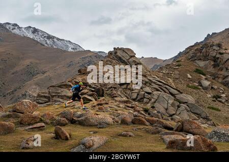 Sportler läuft hoch in den Bergen zwischen den Felsen. Bärtiger Typ joggt in den Bergen. Trailrunning Stockfoto