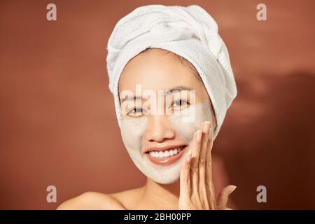 Schöne fröhliche Asiatischen jugendlich Mädchen Anwendung Gesichtsbehandlung Clay Mask. Schönheitsbehandlungen, auf hellen Hintergrund isoliert. Stockfoto