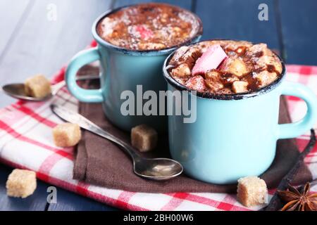 Tassen heißen Kaffee mit Marshmallow auf Serviette mit Klumpen Zucker, Sternanis und Vanillestäbchen auf Farbe Holztisch Hintergrund Stockfoto