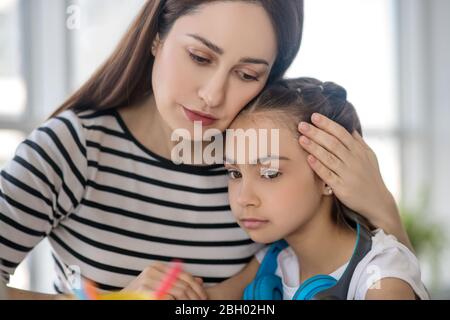 Junge Mutter umarmt traurige Tochter hinter Kopf. Stockfoto