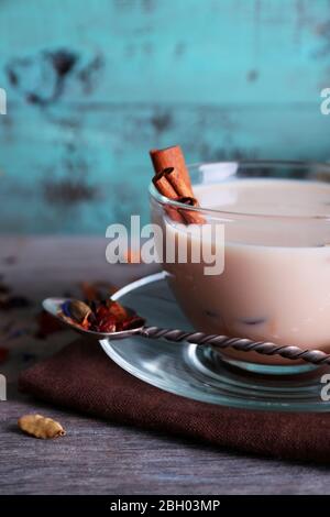 Schwarzer Tee mit Milch und Klumpen Zucker und Gewürze in Glaswaren auf farbigen Holzplanken Hintergrund Stockfoto
