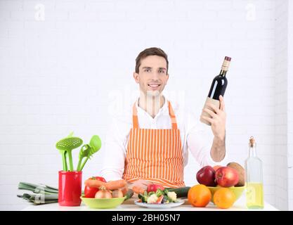 Mann am Tisch mit verschiedenen Produkten und Utensil in der Küche auf weißem Wandhintergrund Stockfoto