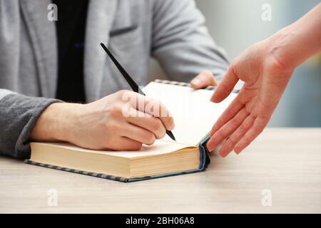 Autor Autograph Signing Autograph in eigenem Buch auf Holztisch auf hellem verschwommenem Hintergrund Stockfoto