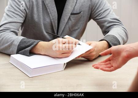 Author Signing Autograph in eigenem Buch am Holztisch auf weißem Plankenhintergrund Stockfoto