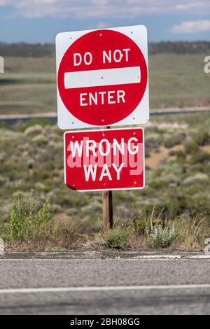 Nahaufnahme eines roten Straßenschilds an der Ecke mit der Aufschrift "nicht betreten, falsche Richtung" vor einer einsamen Landschaft Stockfoto
