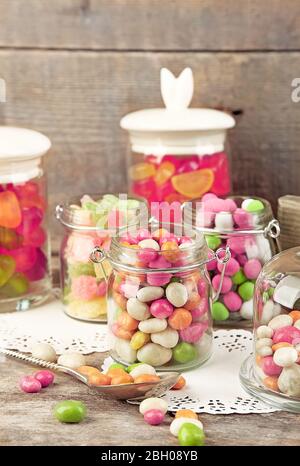Mehrfarbige Bonbons in Glasgefäßen auf Holzhintergrund Stockfoto