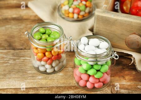 Mehrfarbige Bonbons in Glasgefäßen auf Holzhintergrund Stockfoto