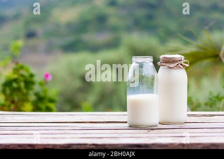 Frische Milch in Glasflasche auf einem Holztisch im Hintergrund der Natur. Kefir, Milch oder Gemüsemilch Stockfoto