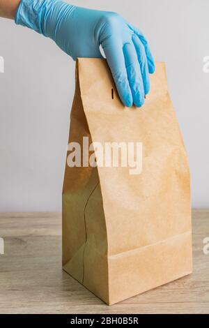 Weibliche Hand in schützenden medizinischen Handschuhen liefert Essen zum Mitnehmen. Lieferdienstkonzept während der Coronavirus-Pandemie Stockfoto