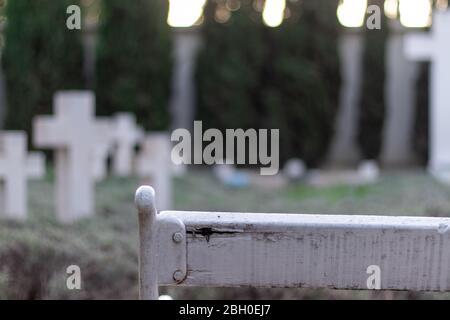 Nahfokus einer alten weißen Ruine Bank, verschwommene Umrisse von weißen Kreuzen in der Ferne. Öffentlicher Friedhof, unmarkierte Gräber gefallener Soldaten aus Stockfoto