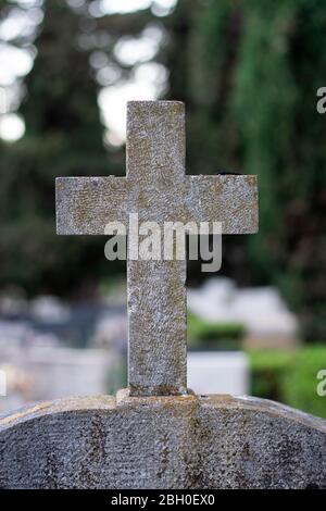 Weißes Steinkreuz mit grün-orangefarbenen Markierungen, die im Laufe der Zeit einen Grabstein auf einem Friedhof markieren Stockfoto