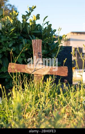 Braunes altes Kreuz auf einem unbekannten Grab, mit Gras und Büschen überwuchert Stockfoto