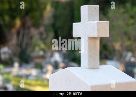 Weißes Steinkreuz mit grün-orangefarbenen Markierungen, die im Laufe der Zeit einen Grabstein auf einem Friedhof markieren Stockfoto