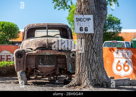 Frontale Nahaufnahme eines alten, zerstörten und rostigen Pickup-Trucks, der in der Nähe eines Baumes geparkt ist, mit Wegweisern zur Route 66, die überall verstreut sind Stockfoto