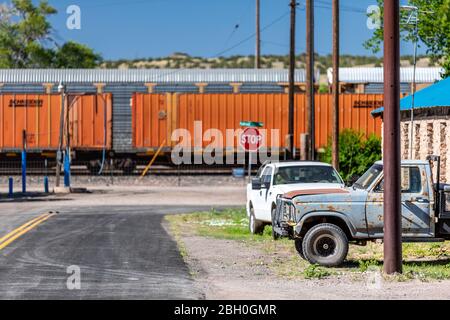 Nahaufnahme einer Hintergasse eines abgelegenen Dorfes in Arizona, mit einem orangen Güterzug, der auf der Eisenbahn vorbeifährt und zwei Pickup-Trucks geparkt Stockfoto