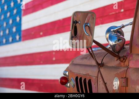 Nahaufnahme eines alten und rostigen roten Pickup-LKW, der gegen eine Backsteinwand geparkt ist, die mit der amerikanischen Flagge bemalt ist Stockfoto