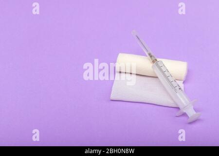 Medizinische Bandage und Spritze auf einem lila Hintergrund. Eine Gaze-Rolle, auf der die Spritze liegt. Dressing für medizinische Zwecke. Platz für Text auf der linken Seite Stockfoto