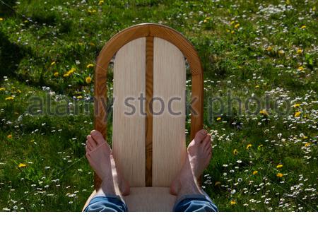 Die Füße eines jungen Mannes, der sich auf einem Stuhl im Sonnenschein im Frühling in einem Garten entspannt. Stockfoto