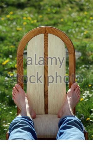 Die Füße eines jungen Mannes, der sich auf einem Stuhl im Sonnenschein im Frühling in einem Garten entspannt.