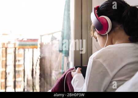 Kleines Mädchen sitzt vor ihrem Haus Balkon mit Headset Videos auf dem Telefon, Home Entertainment für Kinder Konzept, kopieren Raum für t Stockfoto