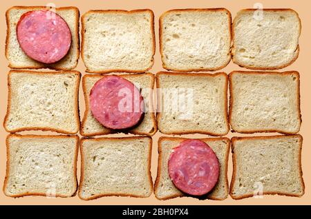 Drei Scheiben Salami und Brot für Sandwiches. Zwölf Brote und geräucherte Wurst auf hellbeigem Hintergrund. Blick von oben. Stockfoto