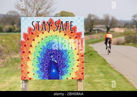 Ein Radfahrer passiert ein Schild Stay Safe in der Nähe einer Farm im Dorf Ratcliffe Culey, Warwickshire während des Coronavirus Covid 19 Ausbruch. Stockfoto