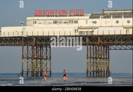 Brighton UK 23. April 2020 - Frühmorgendliche Schwimmer genießen ein Bad im Meer am Brighton Palace Pier an einem schönen heißen sonnigen Tag während der Sperrbeschränkungen während der Coronavirus COVID-19 Pandemie Krise . Die Temperaturen werden voraussichtlich 25 Grad in einigen Teilen des Südostens heute zu erreichen. Quelle: Simon Dack / Alamy Live News Stockfoto