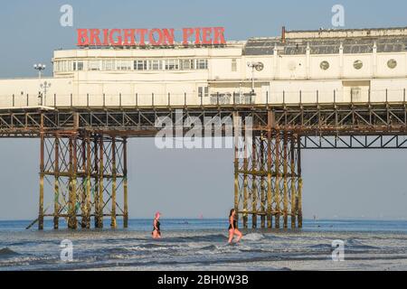 Brighton UK 23. April 2020 - Frühmorgendliche Schwimmer genießen ein Bad im Meer am Brighton Palace Pier an einem schönen heißen sonnigen Tag während der Sperrbeschränkungen während der Coronavirus COVID-19 Pandemie Krise . Die Temperaturen werden voraussichtlich 25 Grad in einigen Teilen des Südostens heute zu erreichen. Quelle: Simon Dack / Alamy Live News Stockfoto