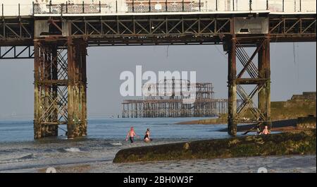 Brighton UK 23. April 2020 - Frühmorgendliche Schwimmer genießen ein Bad im Meer am Brighton Palace Pier mit West Pier hinter an einem schönen heißen sonnigen Tag während der Sperrbeschränkungen während der Coronavirus COVID-19 Pandemie Krise . Die Temperaturen werden voraussichtlich 25 Grad in einigen Teilen des Südostens heute zu erreichen. Quelle: Simon Dack / Alamy Live News Stockfoto