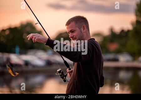 Ein Mann, der vom Flussufer aus auf den Norfolk Broads angeln kann, umgeben von Ferienbooten, die vor Anker liegen. Stockfoto