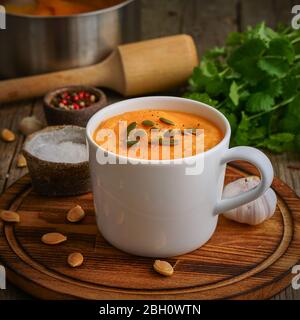 Puppmkin-Sahne-Suppe in Tasse auf braunem Holztisch, Seitenansicht. Diätetisch Stockfoto