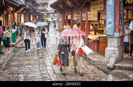 Lijiang, China - 22. September 2017: Menschen auf der Straße der Altstadt an einem regnerischen Tag. Die Altstadt von Lijiang wurde in die UNESCO-Welt Kulturelle He aufgenommen Stockfoto