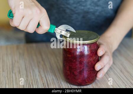 Nahaufnahme einer Frau, die eine Dose in einer Küche mit einem Blechöffner im alten Stil öffnet. Stockfoto