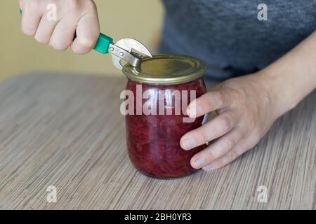 Nahaufnahme einer Frau, die eine Dose in einer Küche mit einem Blechöffner im alten Stil öffnet. Stockfoto