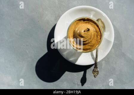 Dalgona Instant-Kaffee Schlagsahne Getränk mit Schokoladenpulver auf der Oberseite in Glas. Hartes Sonnenlicht, Betonhintergrund Stockfoto