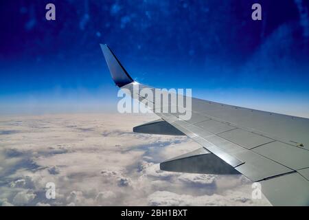 Schöne Panorama-Luftlandschaft - Draufsicht auf den Flügel eines Flugzeugs, blauen Himmel, Wolken und die Erde weit unten Stockfoto