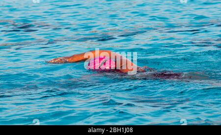 Eine Schwimmerin in einem Freischwimmbad, die mit einer rosa Badekappe im Wasser nach unten schwimmt. Stockfoto