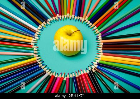 Apfel und Buntstifte sind in einem Kreis auf blauem Hintergrund ausgelegt Stockfoto