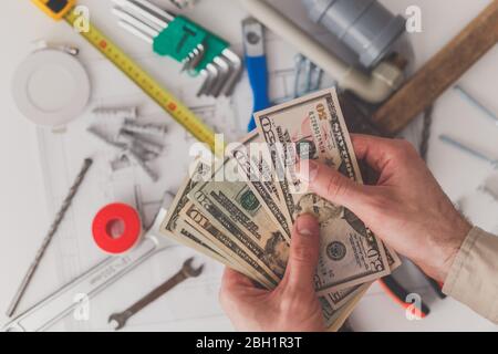 Im Vordergrund zählen die Herren-Hände die Kosten für Reparaturen oder den Bau. Blick von oben. Baumaterial und eine Zeichnung im Hintergrund. Stockfoto