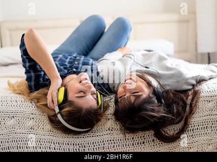 COVID-19-Sperre. Selbstbewusste und optimistische Frauen besten Freundinnen lachen online Musik hören singen und tanzen zusammen im Bett zu Hause in isol Stockfoto