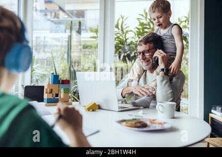 Vater arbeitet von zu Hause aus, telefoniert, während Kinder spielen Stockfoto