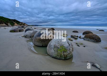 Neuseeland, Otago, Moeraki, Wolken über Cluster von Moeraki Boulder liegen am Koekohe Beach in der Abenddämmerung Stockfoto