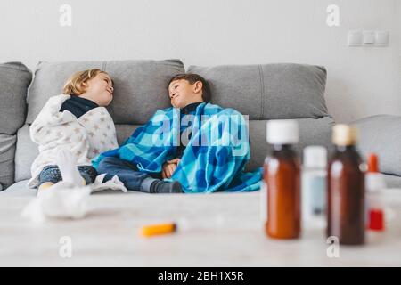 Kranke Geschwister sitzen zu Hause auf der Couch mit Medikamenten auf der Tischplatte im Vordergrund Stockfoto
