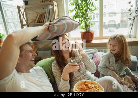 Lachen. Familie verbringen schöne Zeit zusammen zu Hause, sieht glücklich und fröhlich. Mama, Papa und Tochter haben Spaß, Popcorn essen, Fernsehen. Zweisamkeit, häusliche Behaglichkeit, Liebe, Beziehungskonzept. Stockfoto