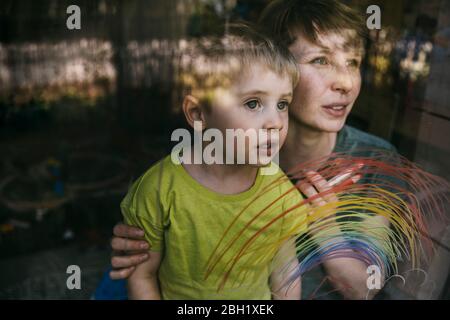 Portrait der Mutter und ihres kleinen Sohnes aus dem Fenster mit gezeichneter Regenbogen Stockfoto